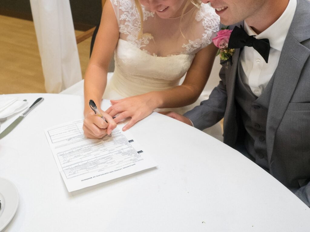 Just-married couple signing a prenup paper on a white table under the lights